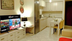 A compact kitchen with a built-in refrigerator, a dining table with chairs, and a flat-screen TV displaying various channels. - Leonidas View (Sparta)