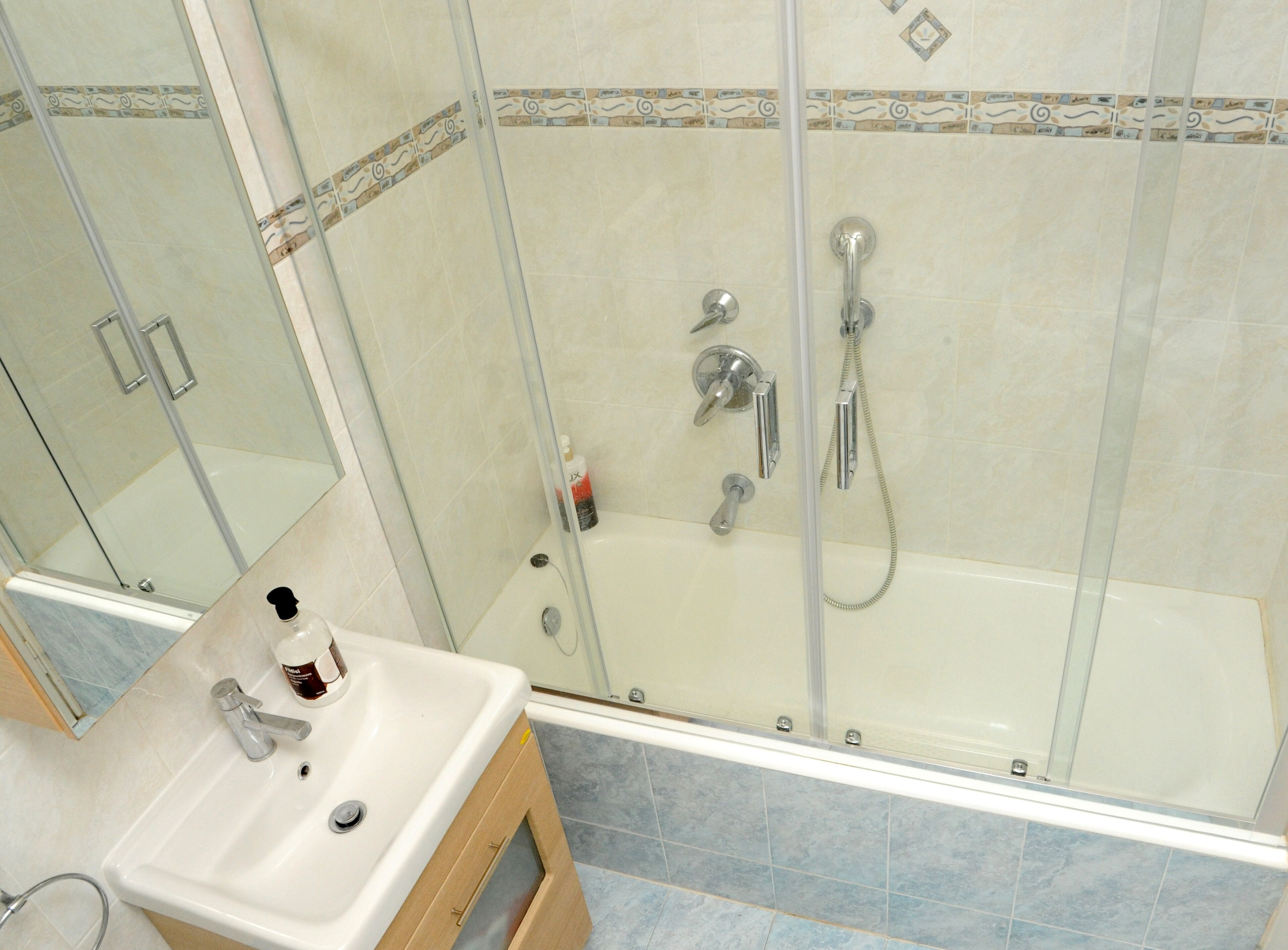 Un baño con ducha de vidrio, lavamanos con espejo y paredes de azulejos.