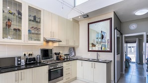 A modern kitchen with light wood cabinets, stainless steel appliances, and a large window providing natural light. - Seaside Village J9 by CTHA (Cape Town)