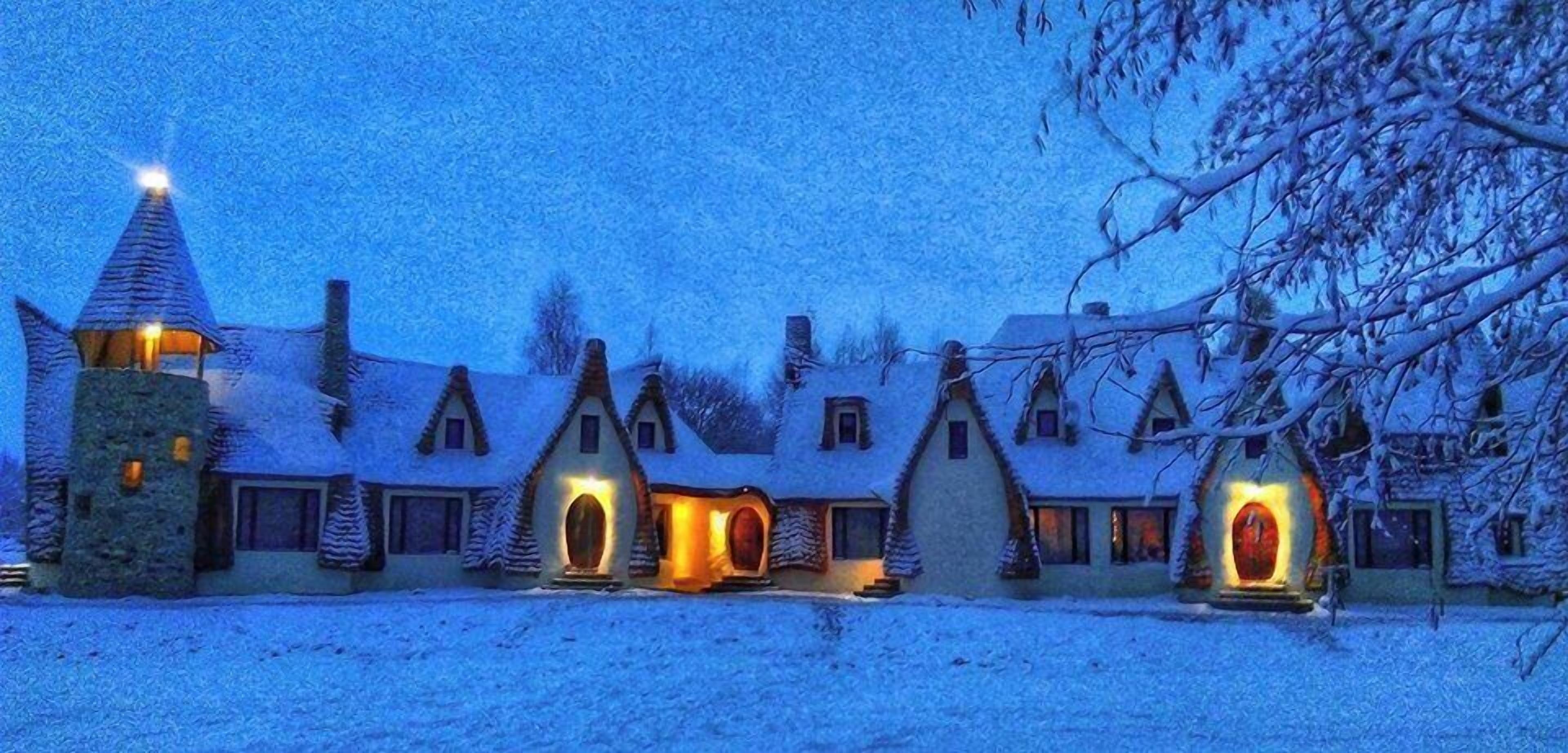 A row of snow-covered cottages with illuminated windows and a central tower.