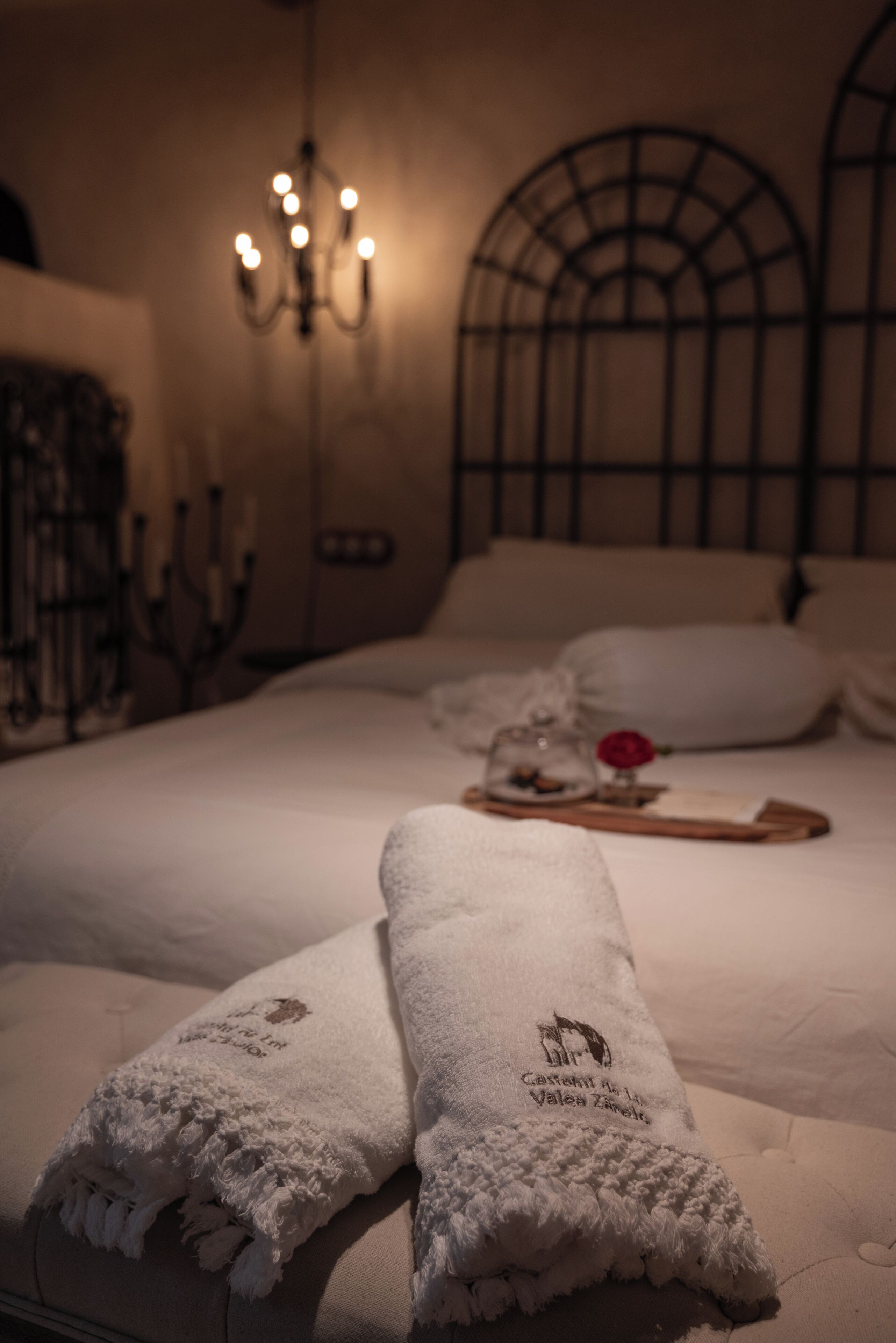 A hotel room with a neatly made bed, a chandelier, and a decorative wall piece.