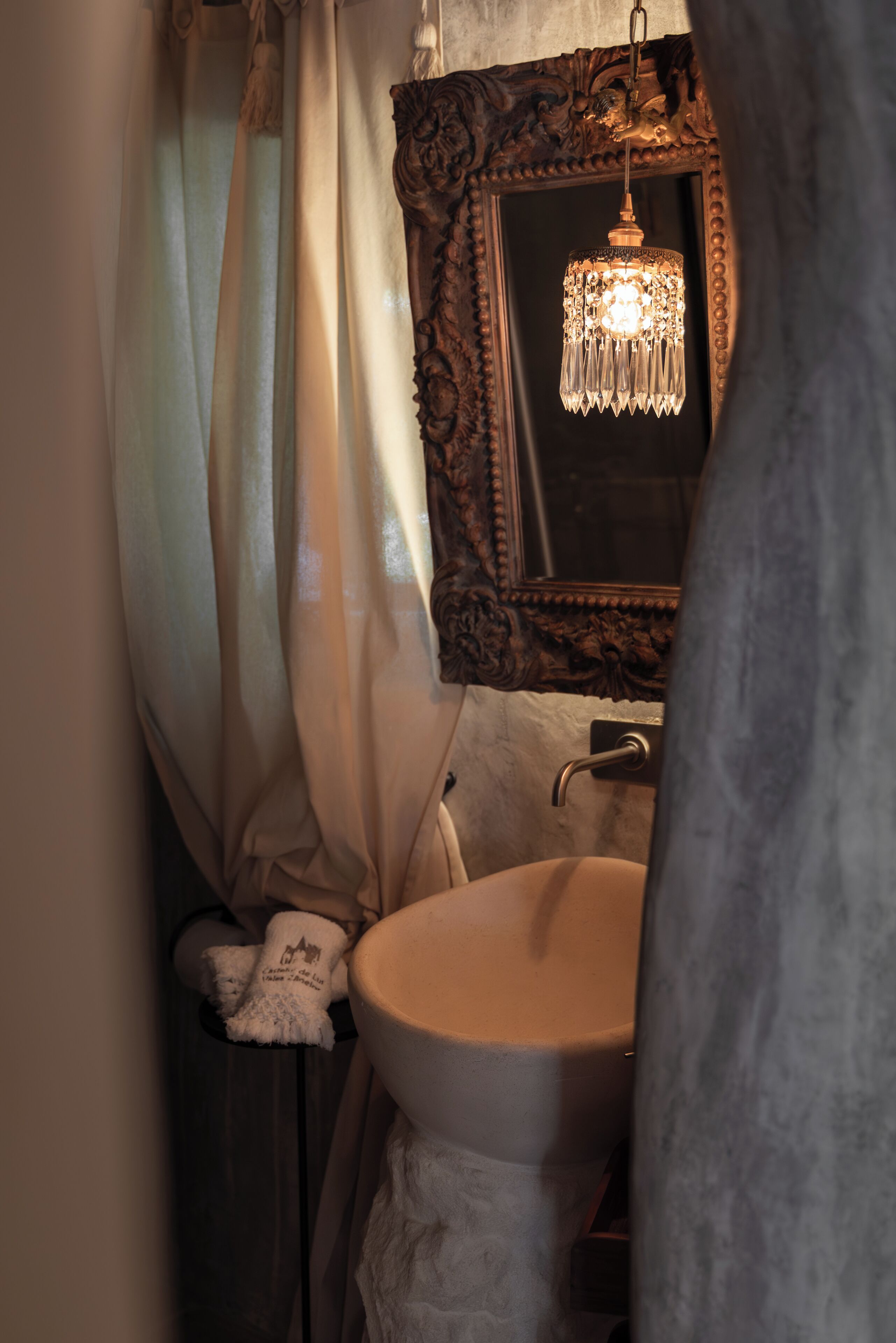 A bathroom with a white sink, a mirror with an ornate frame, and a chandelier.