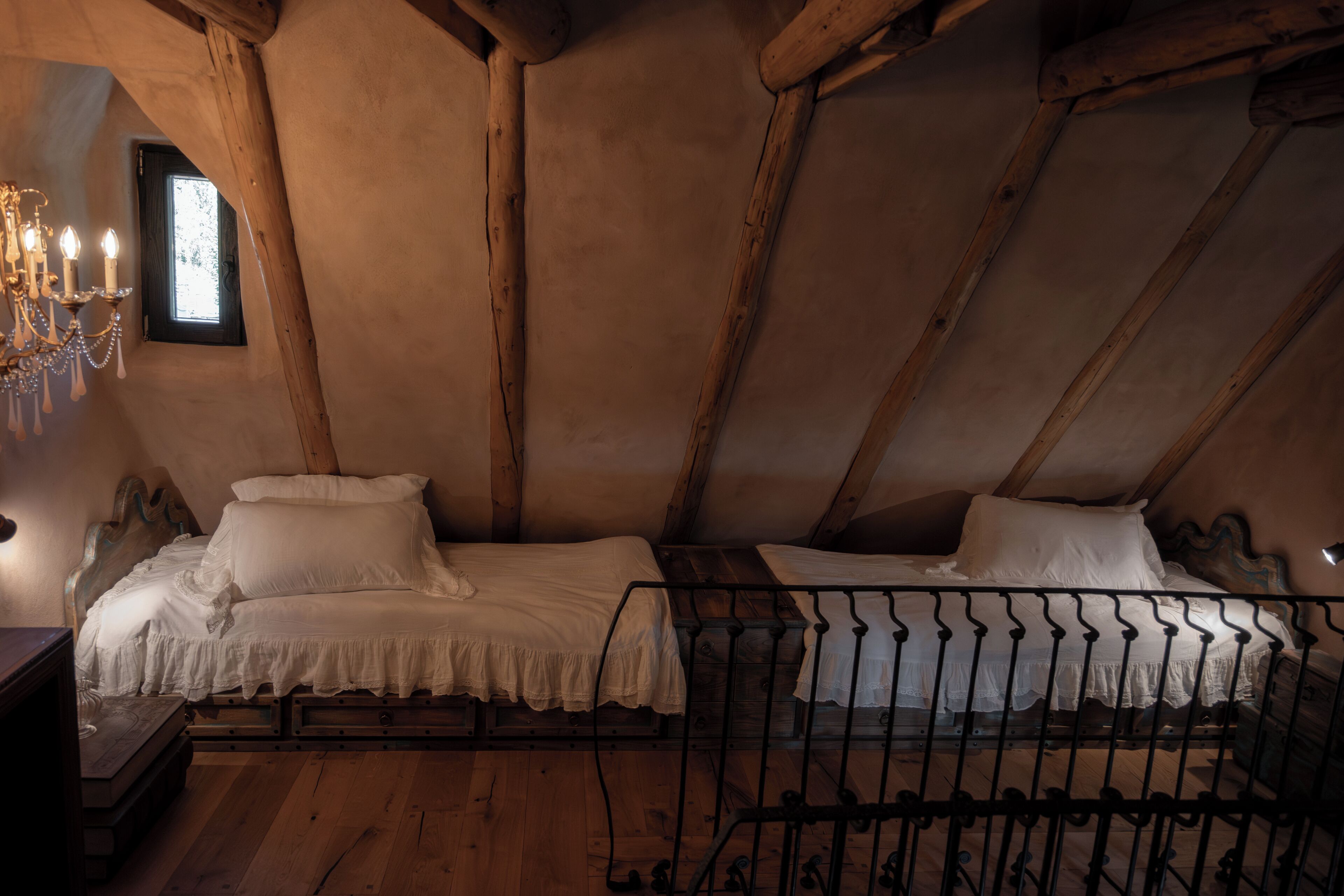 Ein rustikales Schlafzimmer im Dachgeschoss mit Holzbalken, zwei Betten mit weißen Leinen, einer Kandelaber und einem kleinen Fenster.