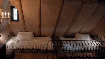 Ein rustikales Schlafzimmer im Dachgeschoss mit Holzbalken, zwei Betten mit weißen Leinen, einer Kandelaber und einem kleinen Fenster.
