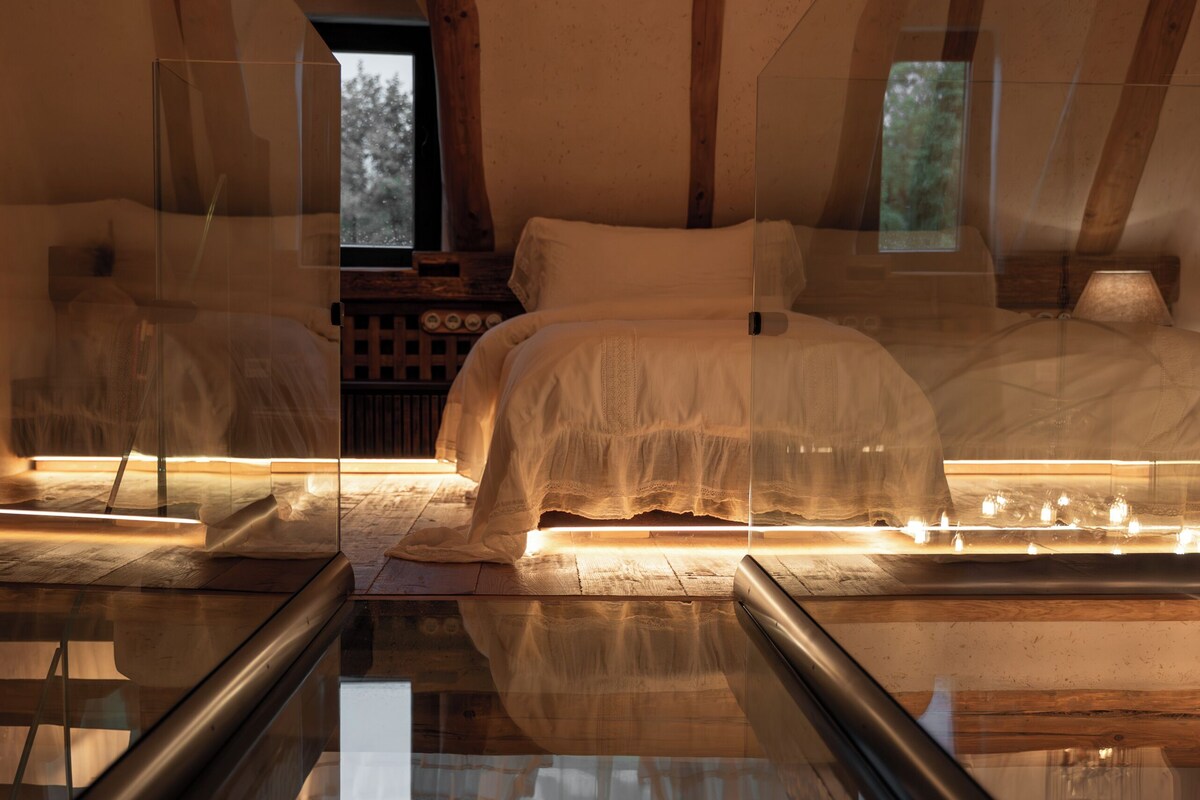 Une chambre avec un plancher en verre, des poutres en bois, un lit et une fenêtre.