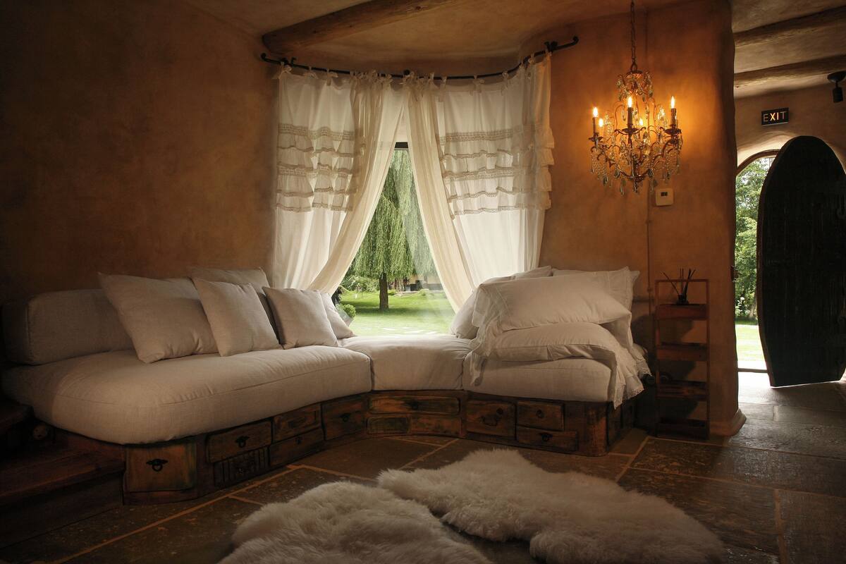 A cozy room with a curved sofa, a chandelier, and a view of greenery outside.