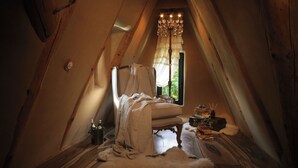 Ein gemütliches Schlafzimmer im Dachgeschoss mit Holzboden, einem großen Fenster mit Vorhang, einer Kristallleuchtreihe und einem Fellteppich.