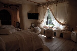Un dormitorio con cama, una ventana con cortinas, un televisor y una mesita con objetos encima.