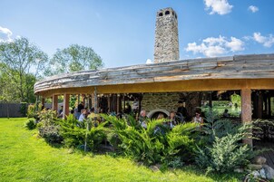 Un área de estar al aire libre de estilo rústico, con pilares de piedra y chimenea de piedra.