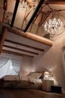 Un dormitorio acogedor con techo de madera, un espejo grande, una araña y una mesita de noche con lámpara.