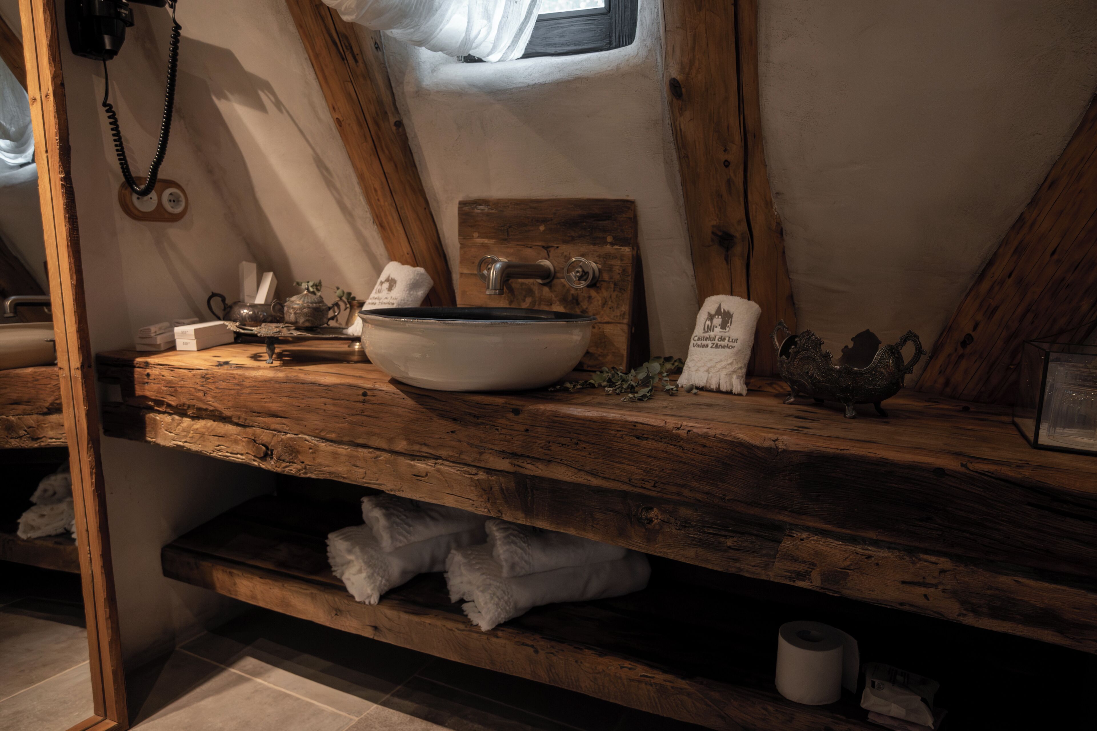 Une salle de bain rustique avec un meuble-lavabo en bois, un évier en céramique blanche et une petite étagère contenant des articles de toilette.