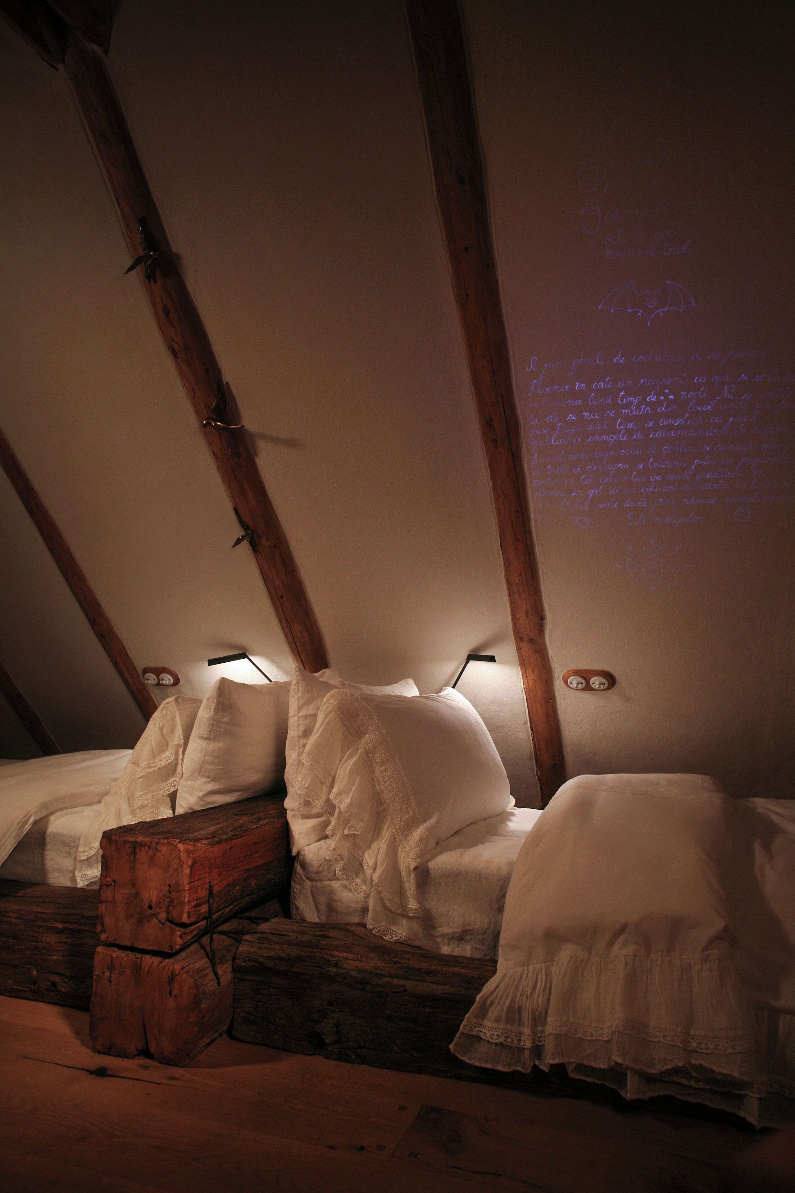 Une chambre mansardée à la lumière tamisée, avec des poutres apparentes, une vieille commode en bois et un lit recouvert de draps blancs.