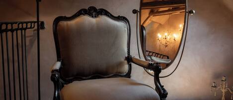 A chair with a mirror, a lamp, and a stack of books in a room with a sloped ceiling and wooden beams.