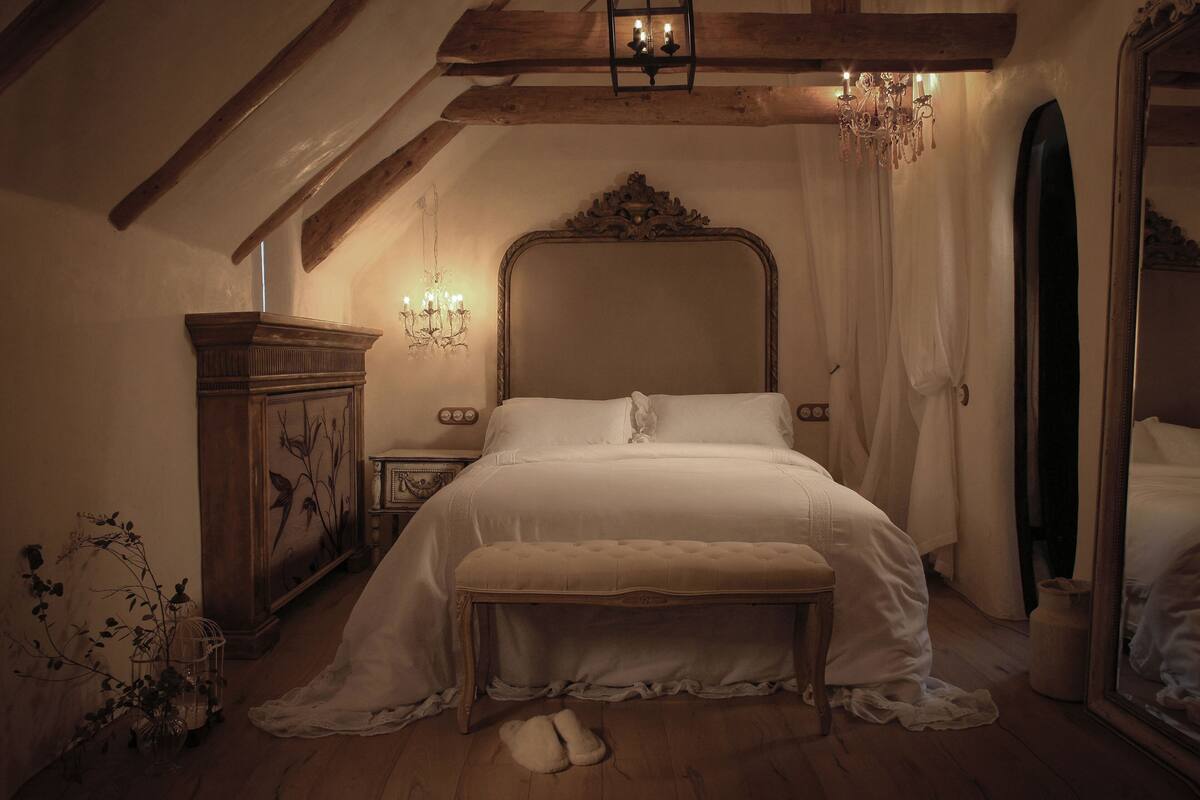A bedroom with a large bed, a wooden bench, a dresser, and a mirror.