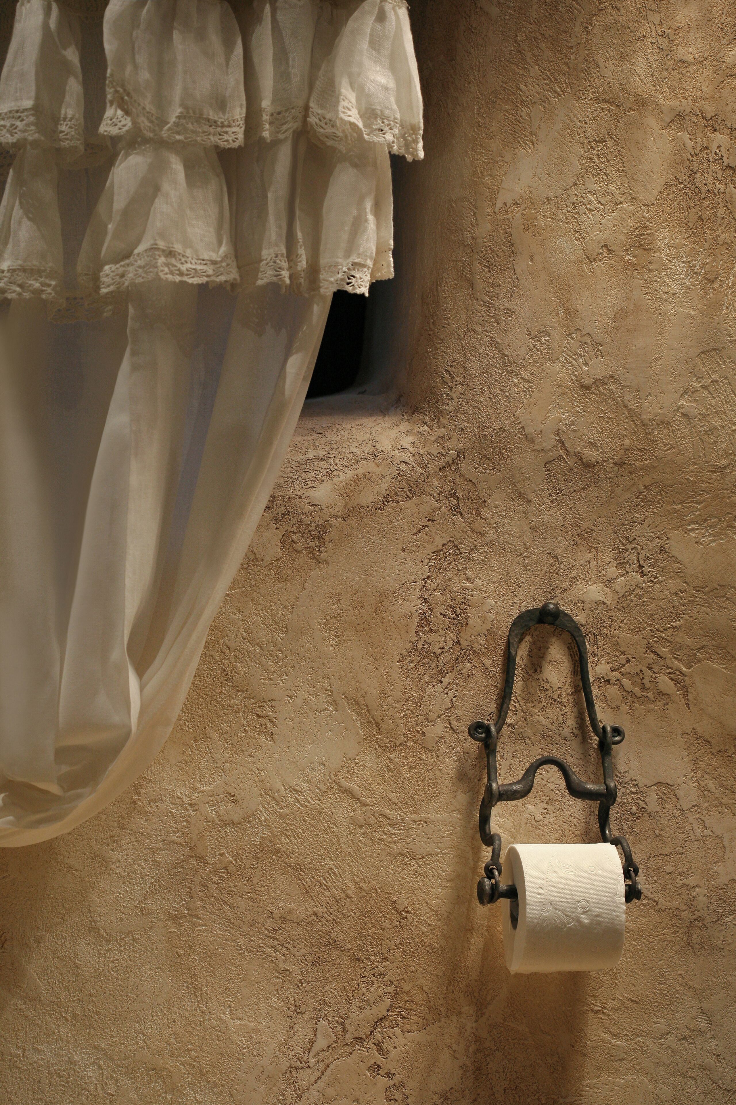 Un baño con pared texturizada, un porta papel higiénico y una cortina translúcida.