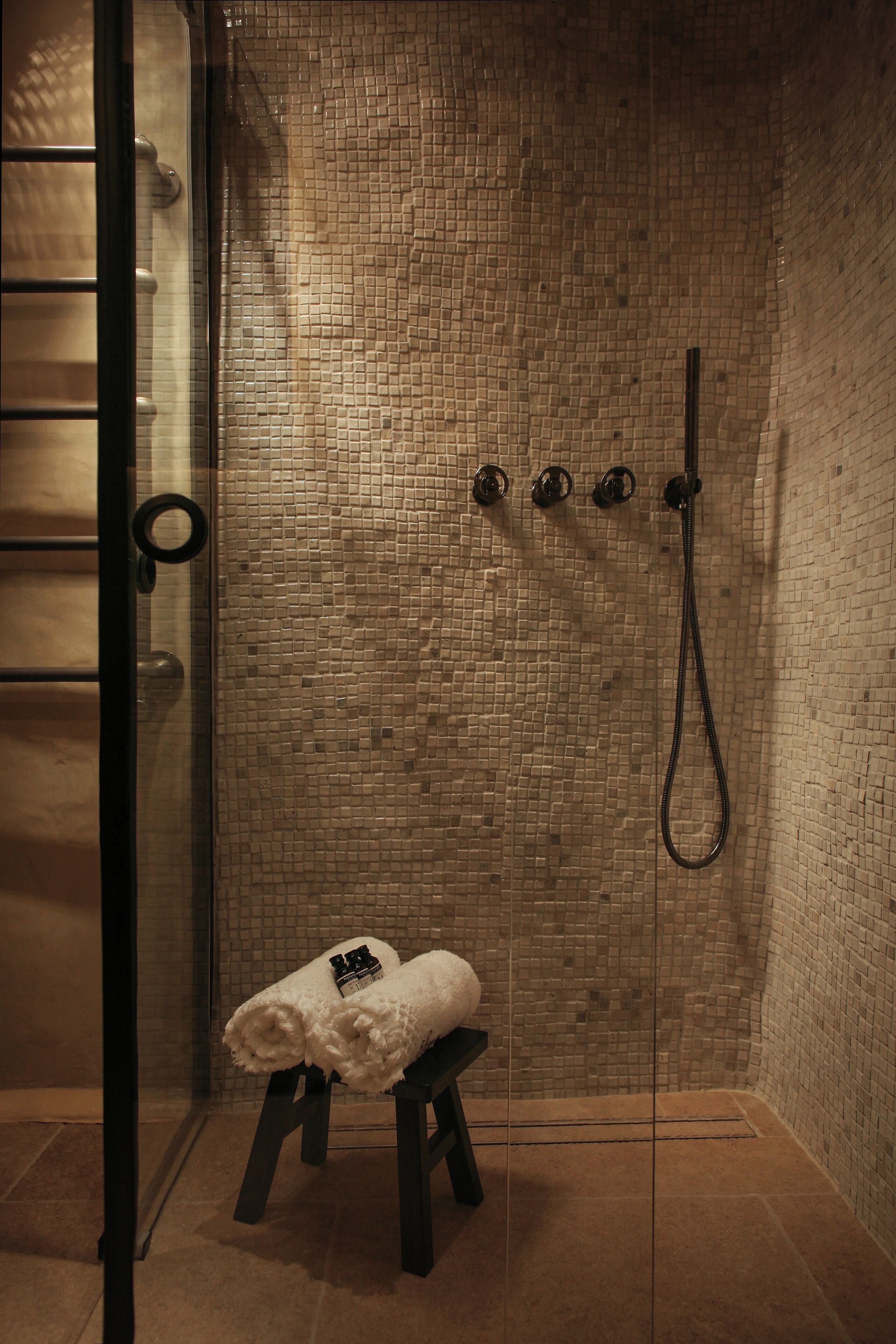 A shower area with a tiled wall, a glass door, and a bench with towels.