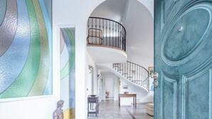 A spacious foyer with a curved staircase, a large blue door, and a wall with abstract art. - Villa Caroline with pool and view (Imperia)