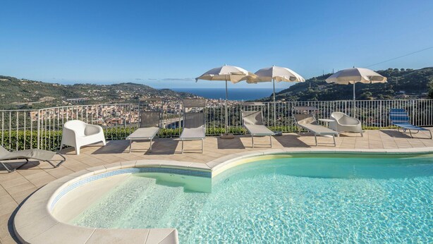 A poolside area with lounge chairs and umbrellas, overlooking a coastal town. - Villa Caroline with pool and view (Imperia)