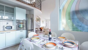 A modern kitchen with white cabinets, a stainless steel refrigerator, and a microwave. There is a dining area with a table set for four, colorful plates, and a bottle of wine. - Villa Caroline with pool and view (Imperia)