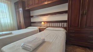 A hotel room with two beds, wooden headboard, a nightstand with a lamp, and a window with curtains. - 213A by R2R Consulting Maximino Apartment (Villaviciosa)