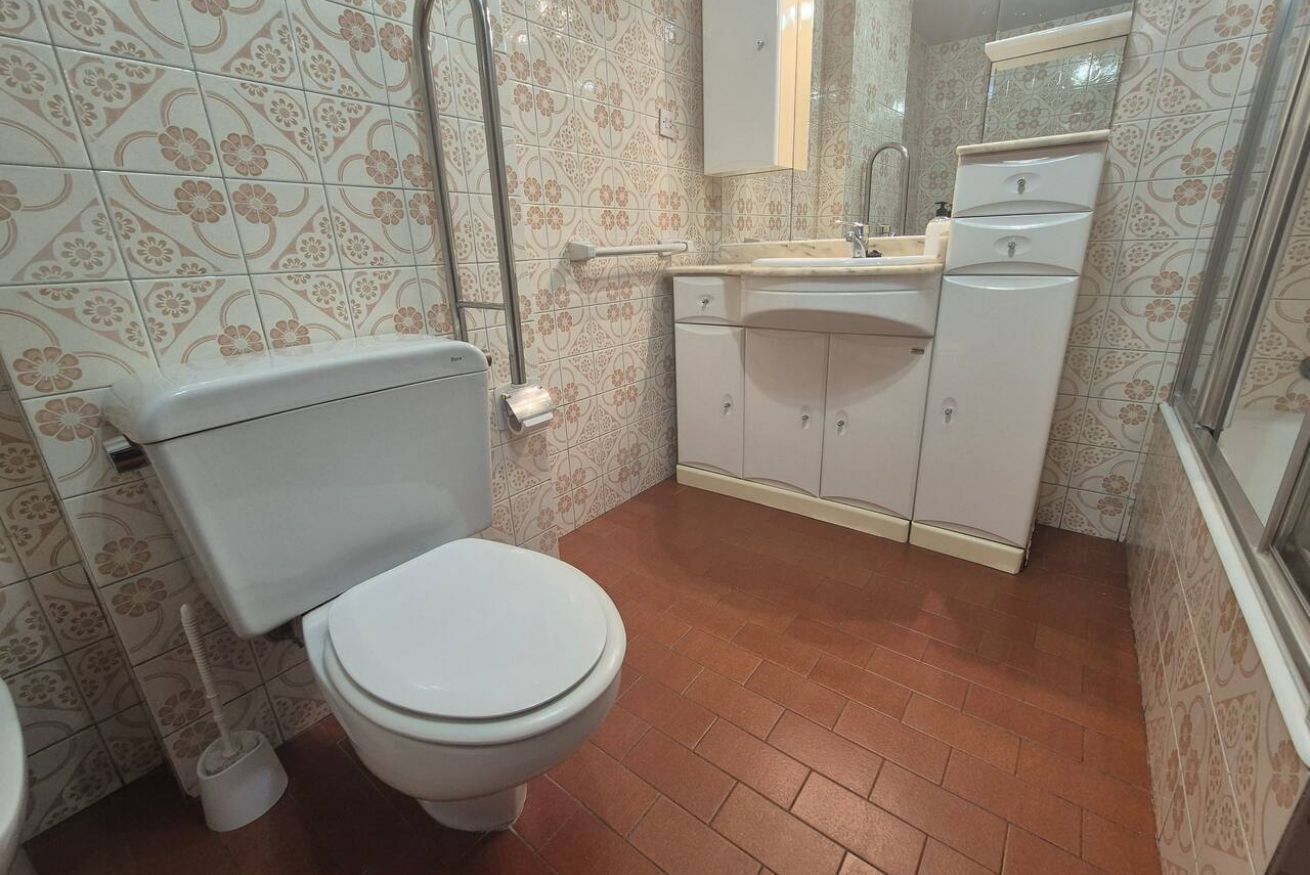 Une salle de bain avec des toilettes, un lavabo, un miroir et des carreaux décorés.
