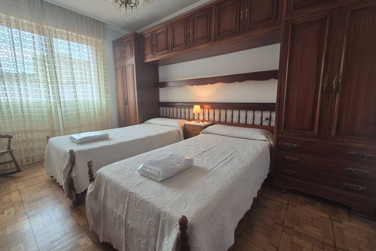 Een hotelkamer met twee bedden, houten kasten, een kroonluchter en een raam met dunne gordijnen.