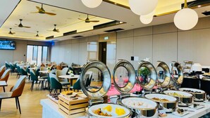 A buffet setup with multiple round serving dishes on a table, ceiling fans, and a modern interior design. - Yishang Hotel  (Chengmai)