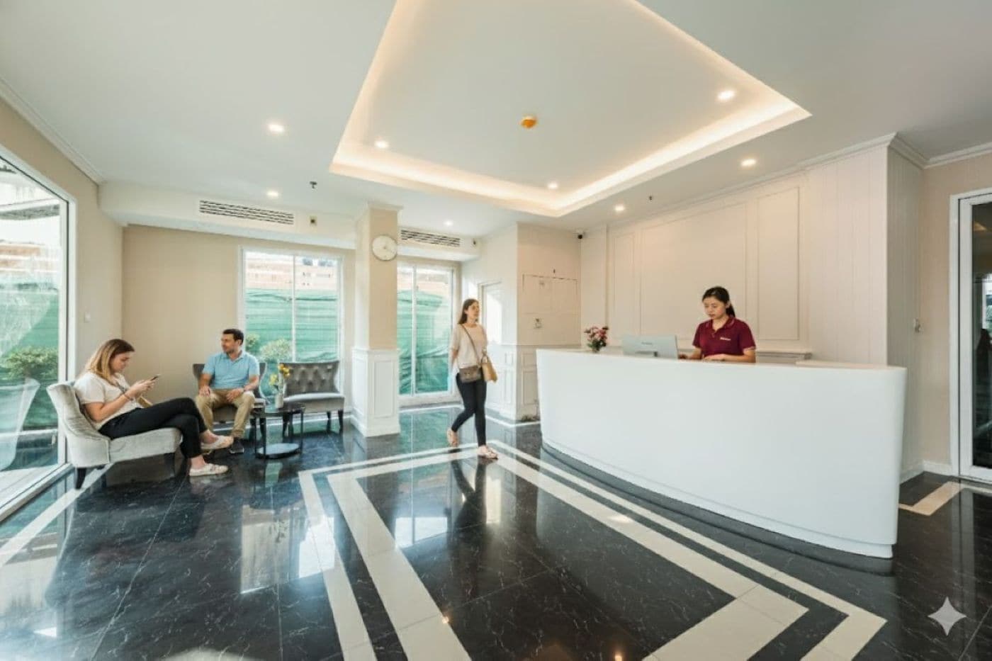 A modern hotel lobby with a reception desk, seating area, and large windows.