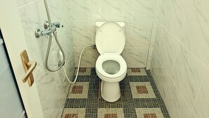 Un baño con inodoro, ducha y suelo de baldosas.