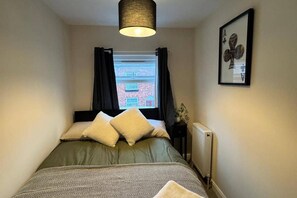 A bedroom with a bed, a radiator, a window with curtains, and a framed picture on the wall. - Winsford Woodford Cottage - Sleeps 6 - Pets Ok (Winsford)