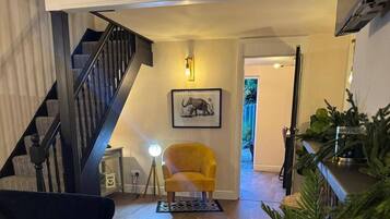 Una escalera que lleva al segundo piso, un sillón amarillo, un cuadro con un elefante enmarcado, y una planta en un estante.