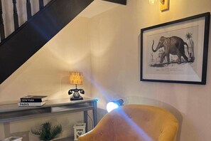 A room with a staircase, a lamp, a chair, a framed picture, and a small table with books. - Winsford Woodford Cottage - Sleeps 6 - Pets Ok (Winsford)