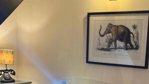 A framed elephant illustration on a wall, a lamp, and a desk with a telephone. - Winsford Woodford Cottage - Sleeps 6 - Pets Ok (Winsford)
