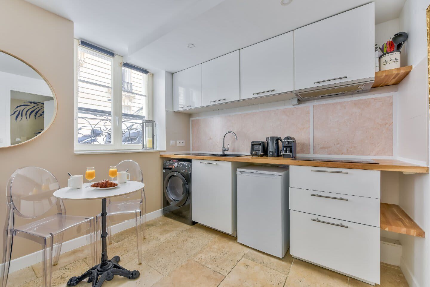 A compact kitchen with white cabinets, a washing machine, a coffee maker, and a dining area with a table and chairs.