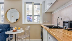 A compact kitchen with a sink, a coffee maker, and a dishwasher. There's a round mirror on the wall and a window with a view of the street. - Atelier d'artiste a Saint Germain (Paris)