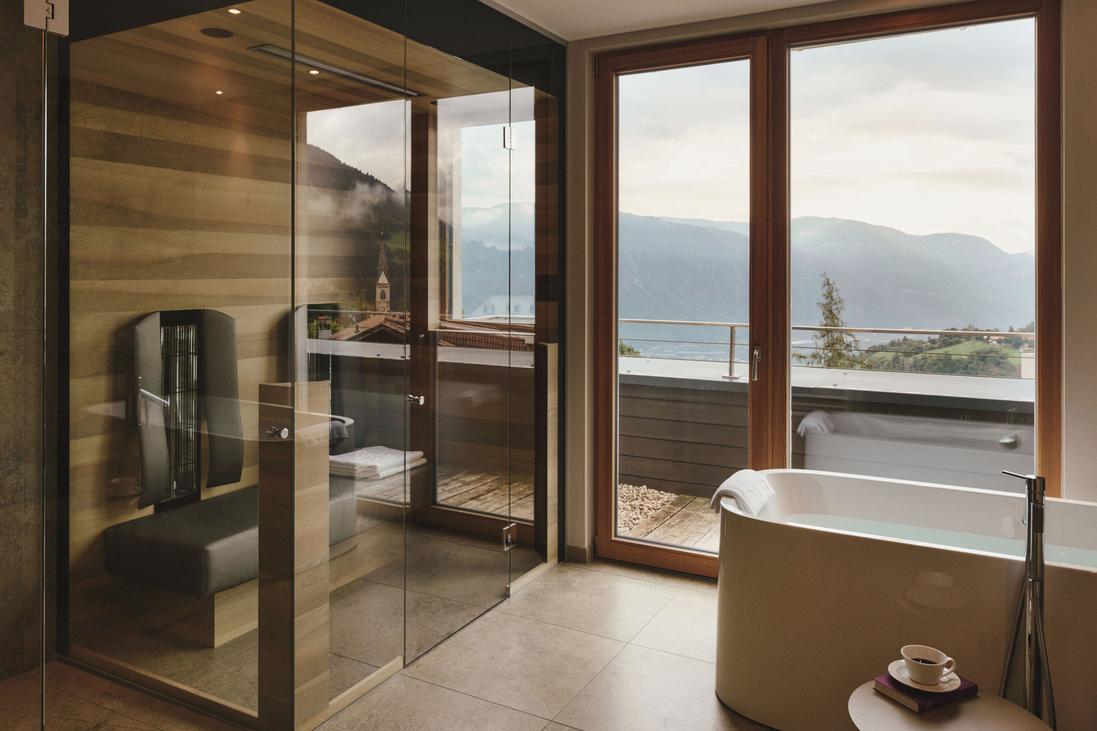 Un baño moderno con cabina de ducha de vidrio, bañera y vistas a montañas a través de grandes ventanales.