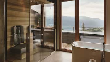 Un baño moderno con cabina de ducha de vidrio, bañera y vistas a montañas a través de grandes ventanales.