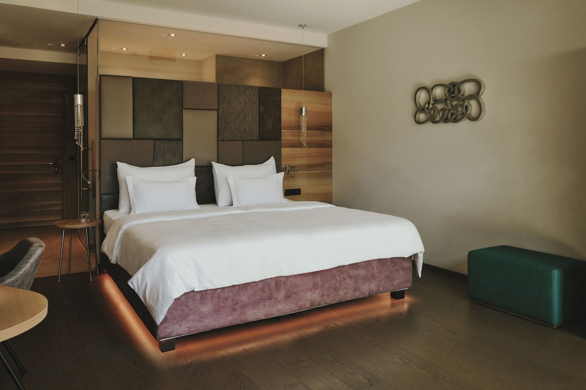 Quarto de hotel moderno com uma cama grande, um espaço para sentar e uma peça decorativa na parede.