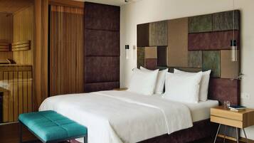 A modern hotel room with a large bed, a bench, a nightstand, and a wooden wardrobe.
