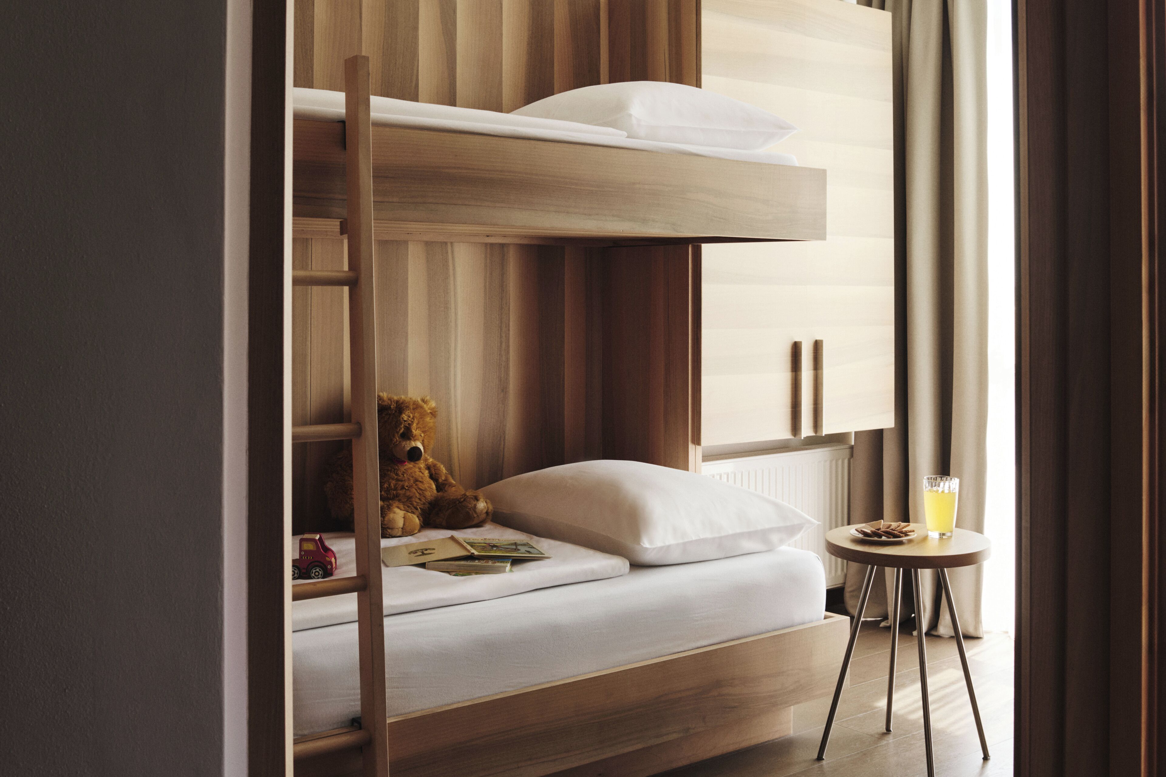 A bunk bed with a teddy bear, a small table with a glass of juice, and a radiator.
