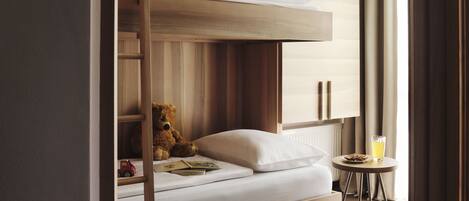 A bunk bed with a teddy bear, a small table with a glass of juice, and a radiator.