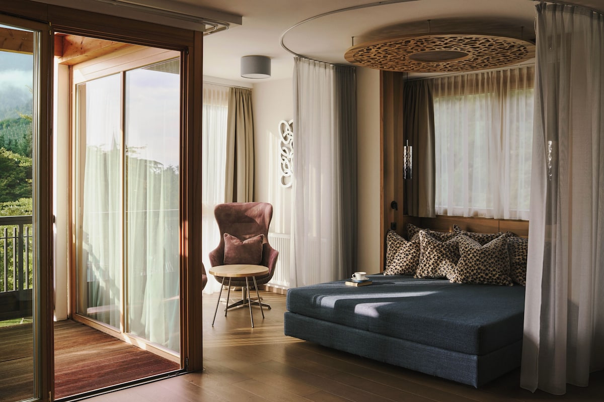 Quarto com cama grande, uma cadeira e vista para o exterior.