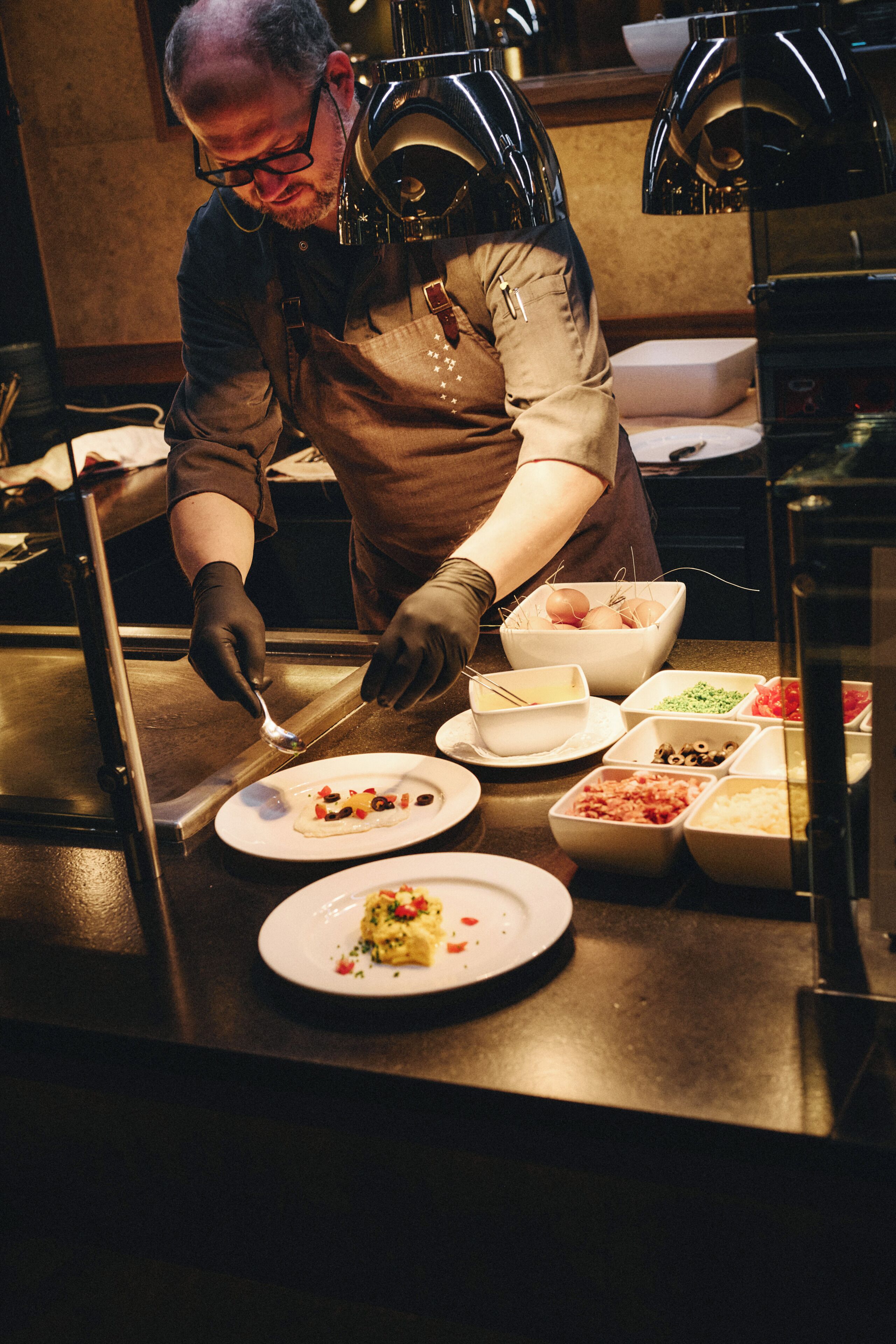 Una persona sirviendo comida en un bufé con varios platos y utensilios a la vista.
