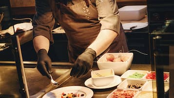 Una persona sirviendo comida en un bufé con varios platos y utensilios a la vista.
