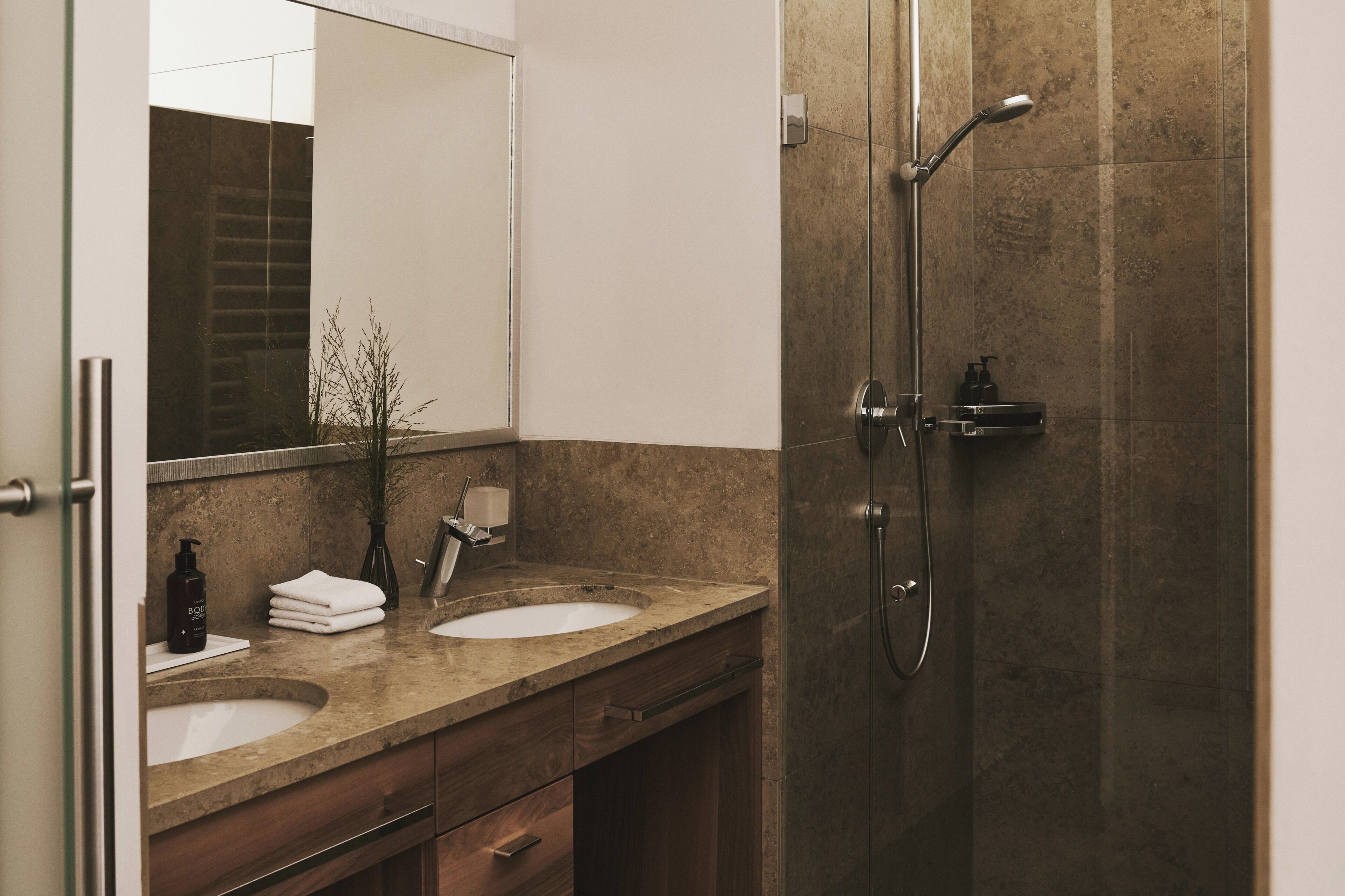 Baño con lavamanos doble, espejo, cabina de ducha y toallero.