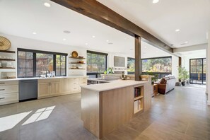Une cuisine spacieuse dotée d’un îlot central, de meubles en bois et de grandes fenêtres offrant une vue sur l’extérieur.