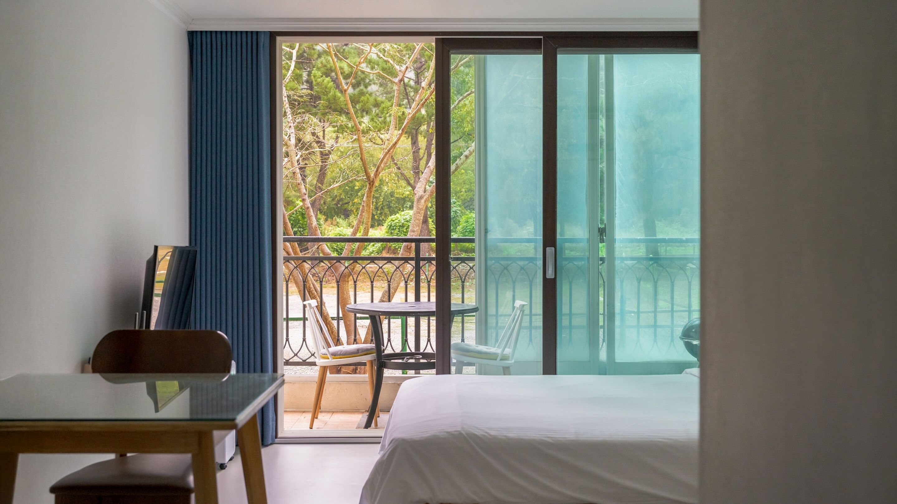 A hotel room with a bed, a desk, and a balcony with a table and chairs.