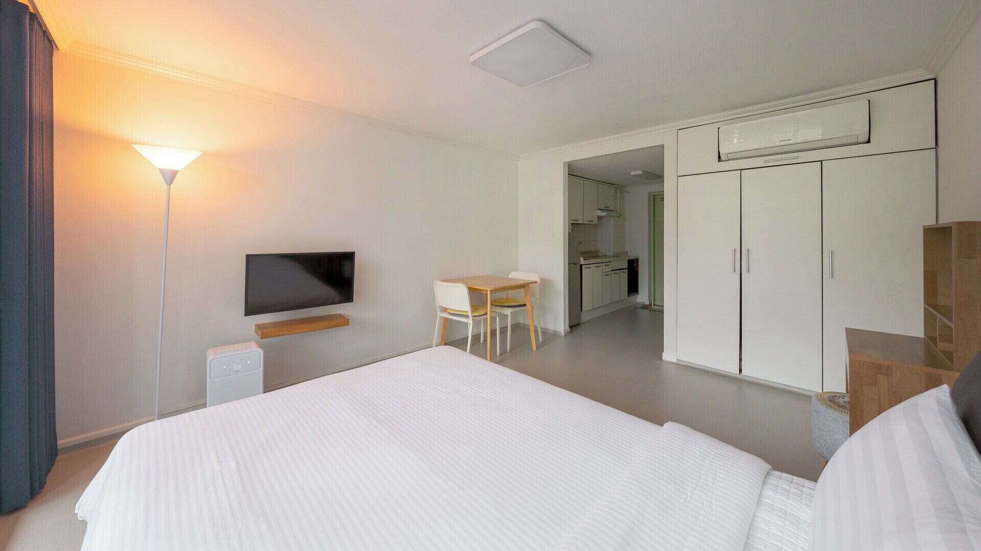 A hotel room with a bed, a desk, a TV, and a kitchenette.