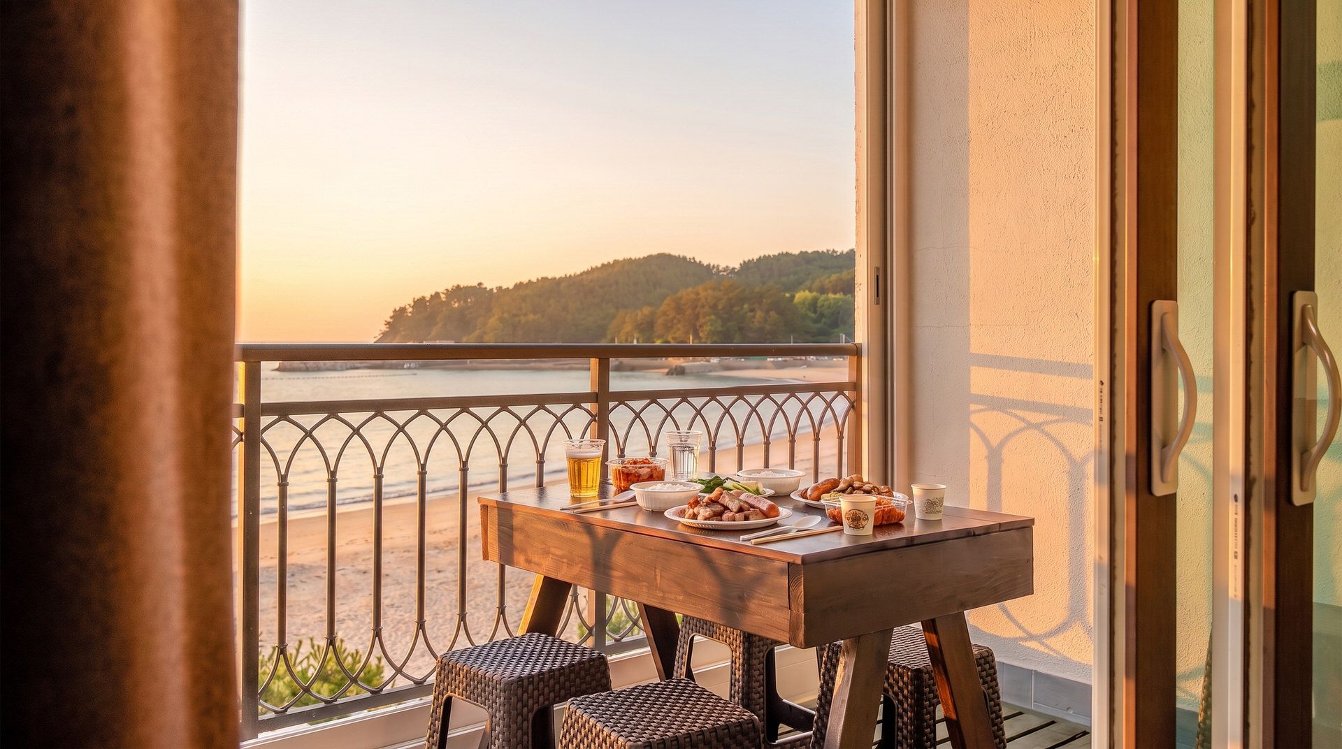 A balcony with a table set for dining, overlooking a beach and forested area.