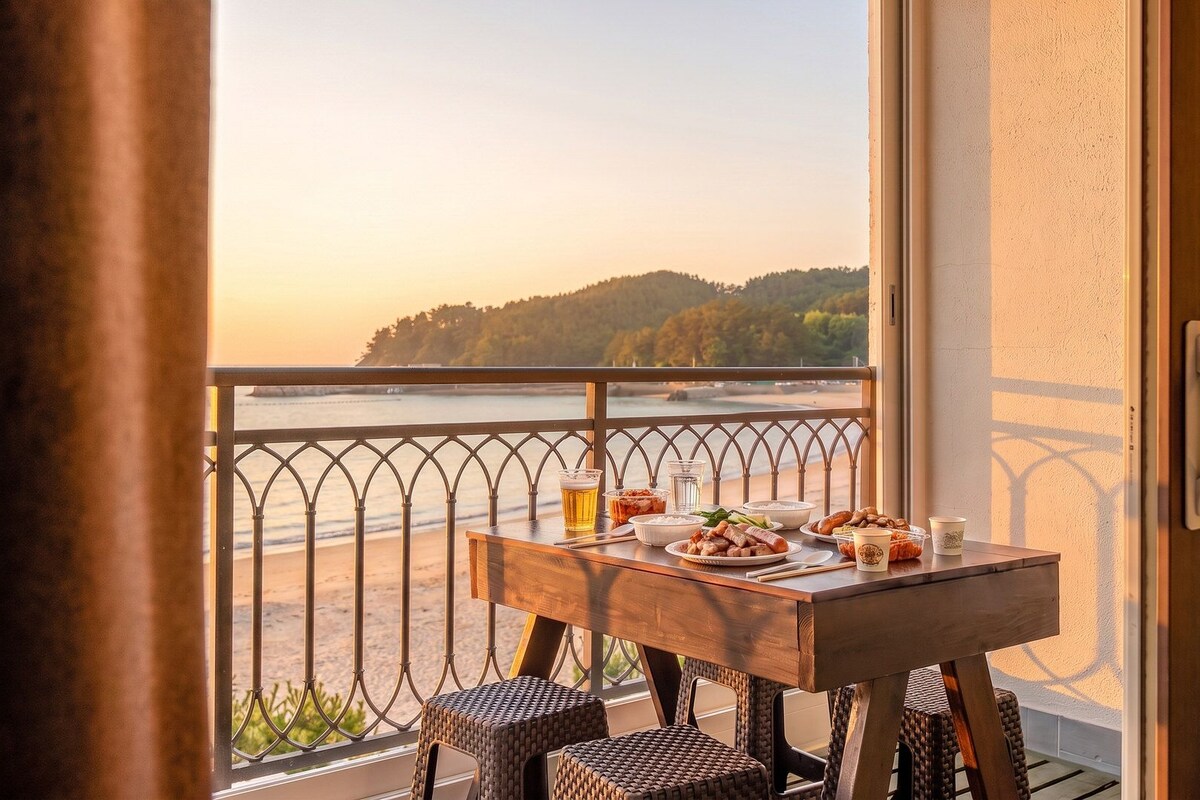 A balcony with a table set for dining, overlooking a beach and forested area.